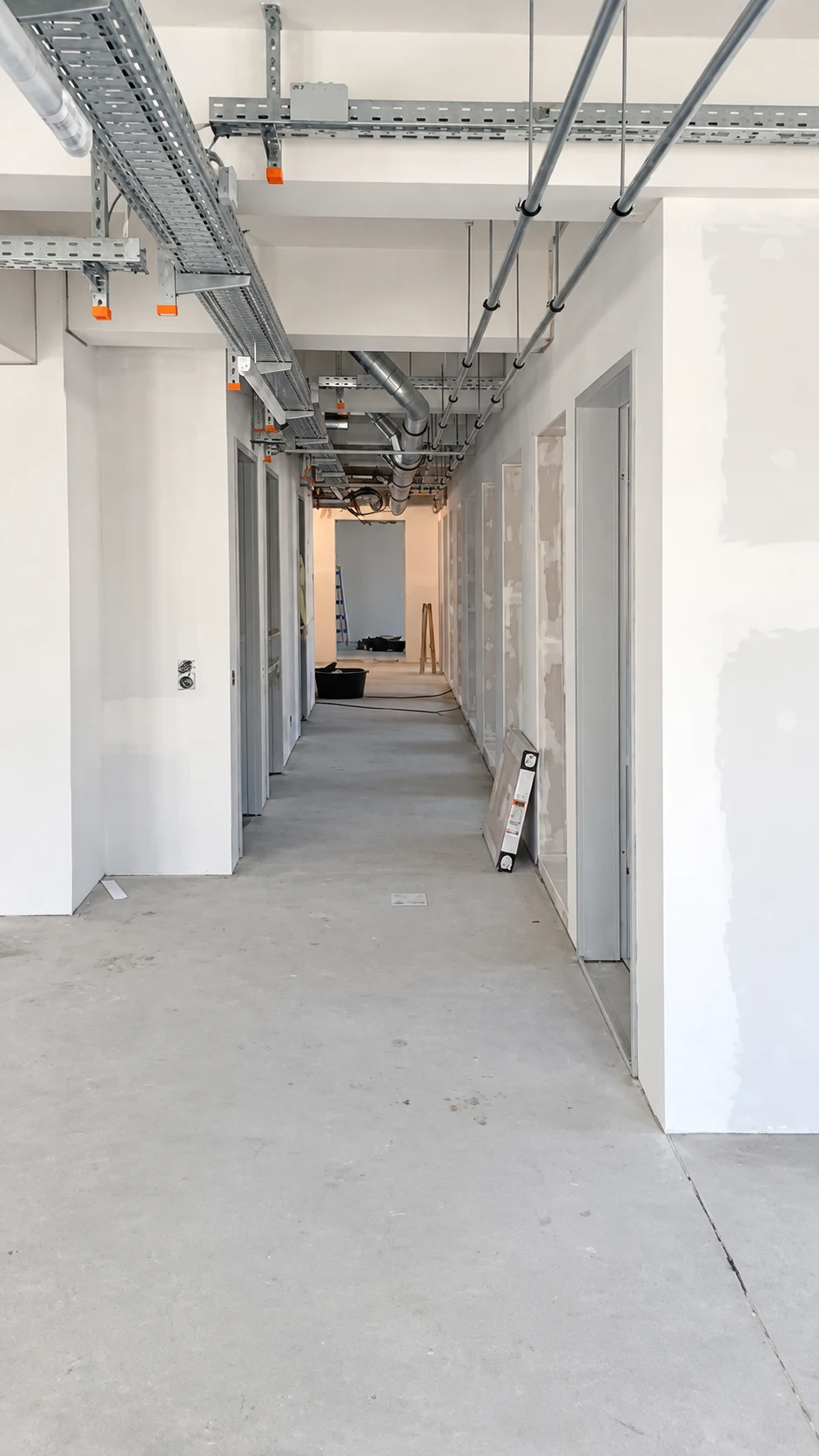 Flur im Ausbau mit offenen Deckeninstallationen und Gipskartonwänden